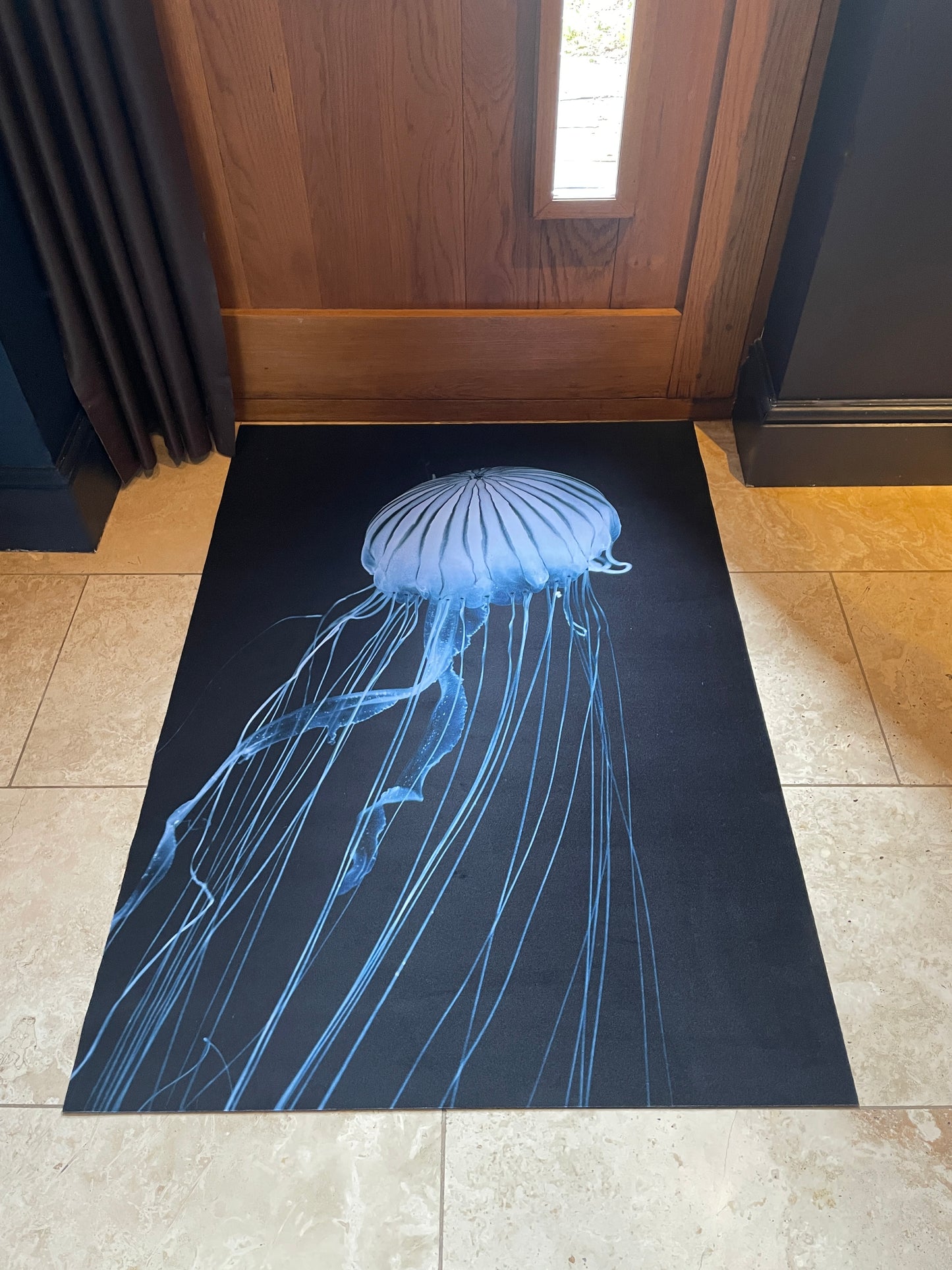 Black doormat with a blue jellyfish design on a tiled floor.
